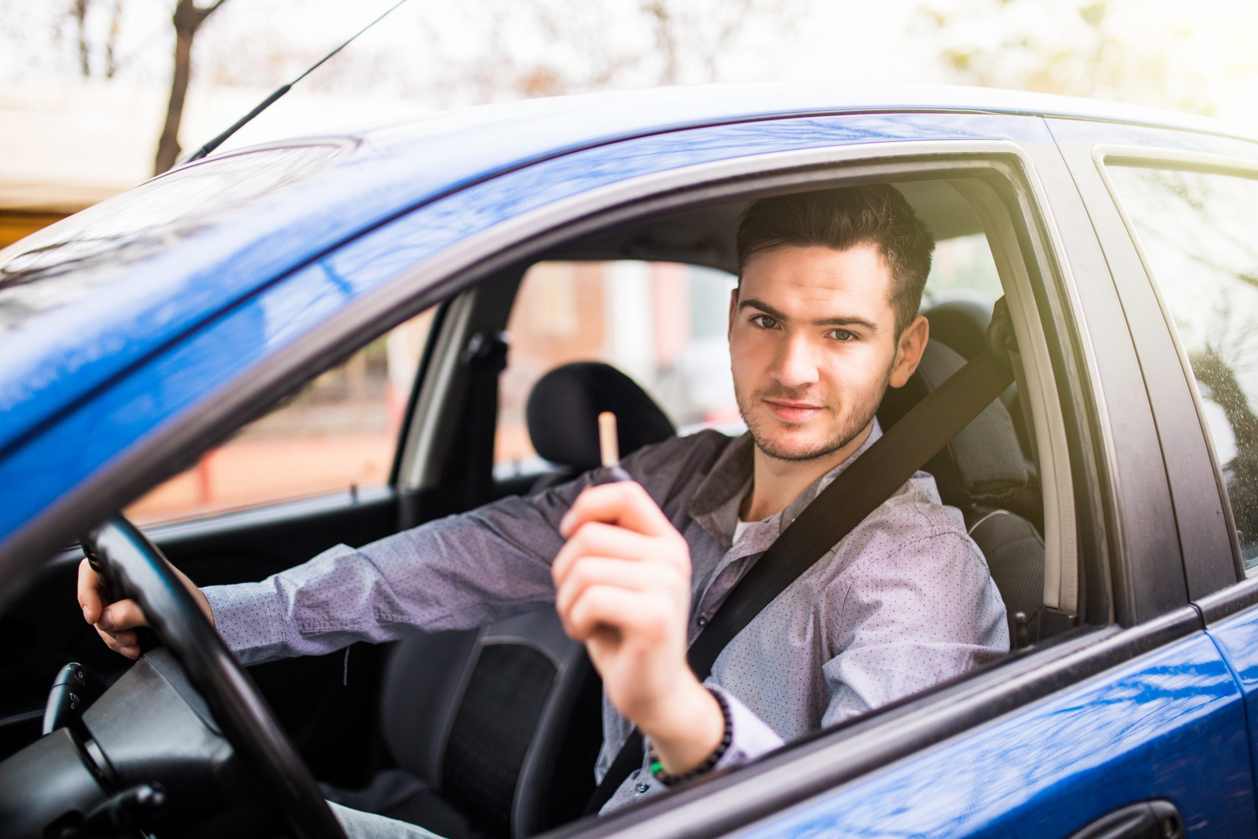 young handsome man driving his new car holding out keys scaled